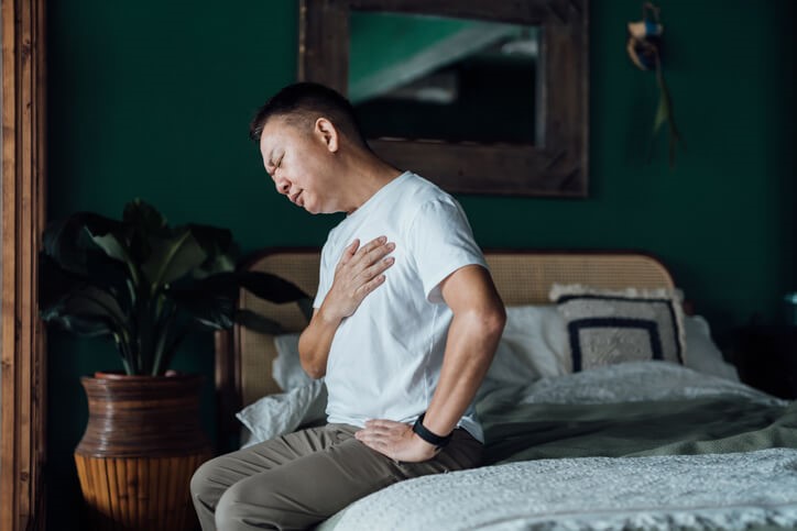 Man sitting on a bed holding his chest